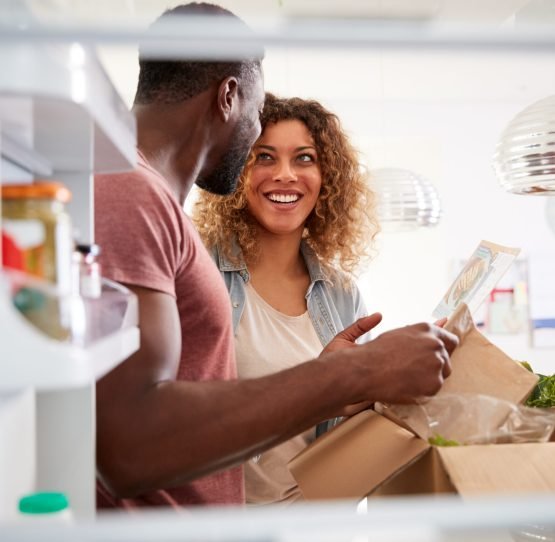 View Looking Out From Inside Of Refrigerator As Couple Unpack Online Home Food Delivery